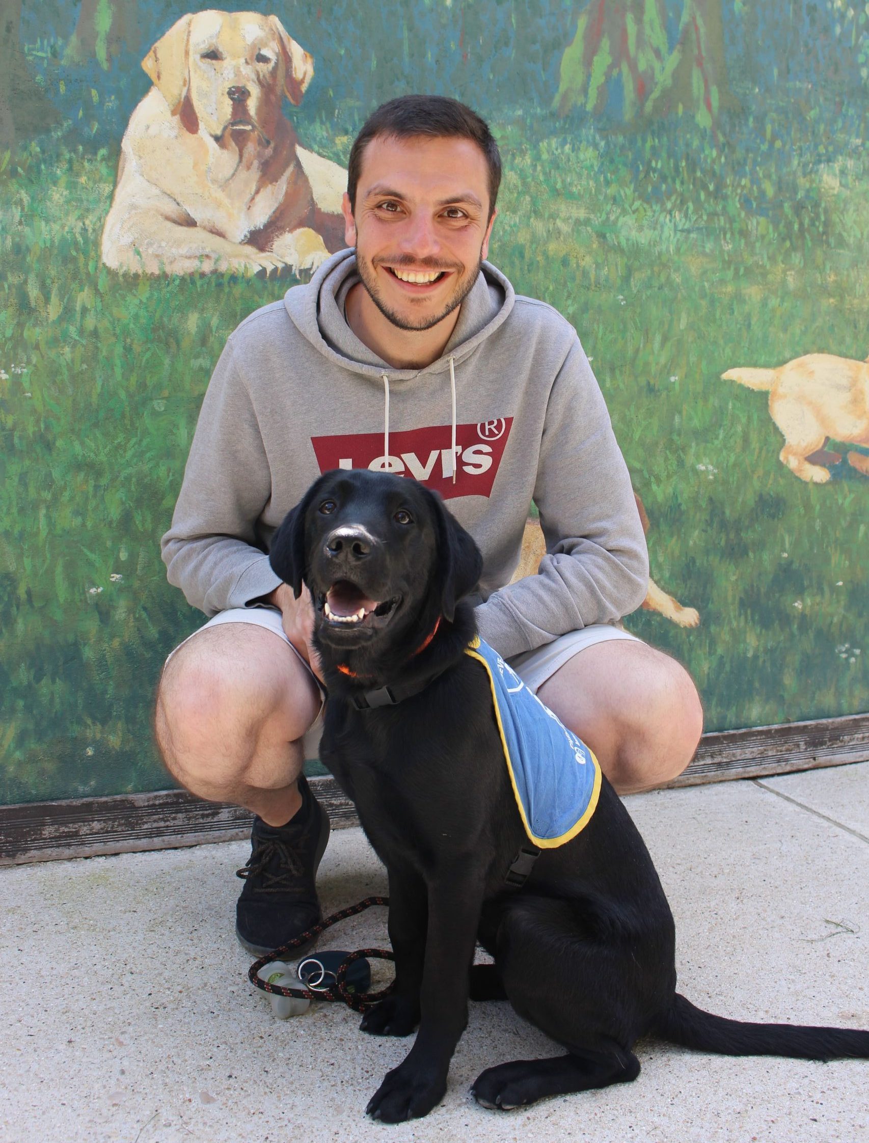 Alexandre et son élève chien guide Ubbay devant la fresque de l'Ecole