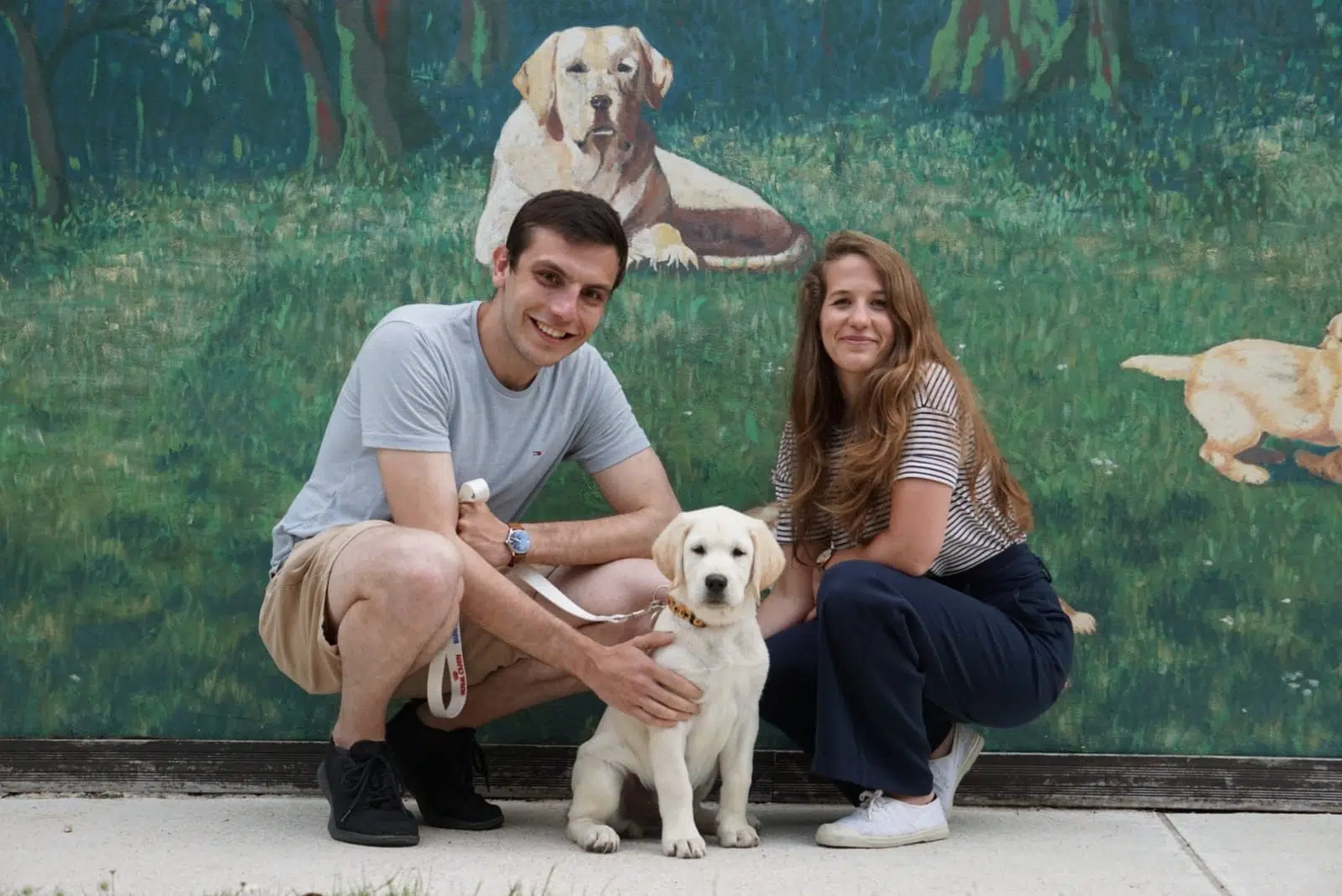 Alexandre et Julie, famille d'accueil, avec Shaggy chiot, devant la fresque de l'Ecole